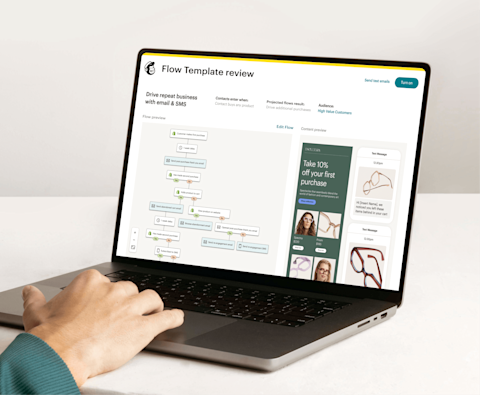 Image of a person sitting at a desk, looking at a laptop screen displaying Mailchimp’s Automation Flow Template review feature. The feature shows a preview of an automation journey and an abstract view of email and SMS interfaces from the fictitious brand Escultura.