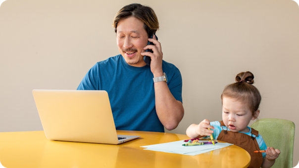 A business owner seated at a table, working from home and looking after a child while they speak 1:1 with a Mailchimp customer success representative.